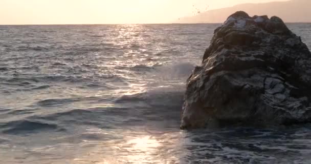 Vista de las olas rodadas en la línea de la costa del mar con enorme roca al atardecer — Vídeos de Stock