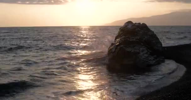 Vista de las olas rodadas en la línea de la costa del mar con enorme roca al atardecer — Vídeos de Stock