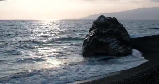 Vista de las olas rodadas en la línea de la costa del mar con enorme roca al atardecer — Vídeos de Stock