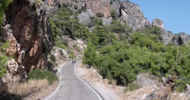 Dos jóvenes caminatas turísticas con mochilas pasando por la carretera en las montañas — Vídeo de stock