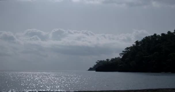 ギラギラと輝く地平線上の島と海の表面の小石の海岸ライン — ストック動画