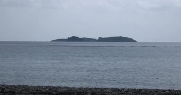 Linea di costa di ciottoli con ascolto e scintillante superficie del mare con isola su Horizon — Video Stock