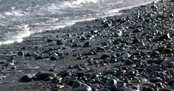 반짝 반짝이 바다 표면와 자갈 해안 라인에 압 연 파도 — 비디오