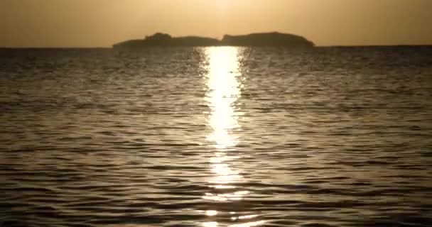 Skimrande havet ytbehandlar vid soluppgången med suddiga ön på en bakgrund — Stockvideo