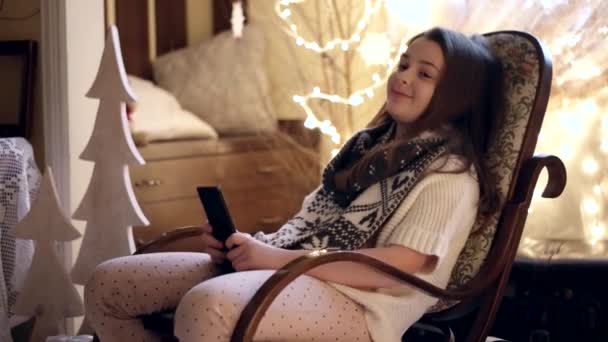 Beautiful Little Girl is Sitting in the Rocking Chair and Use Mobile Phone — Stock Video