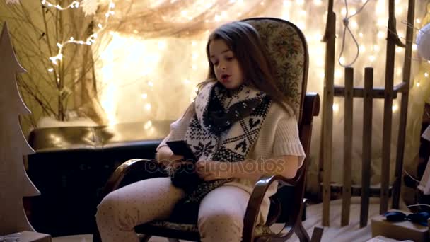 Schönes kleines Mädchen sitzt im Schaukelstuhl und benutzt Handy — Stockvideo