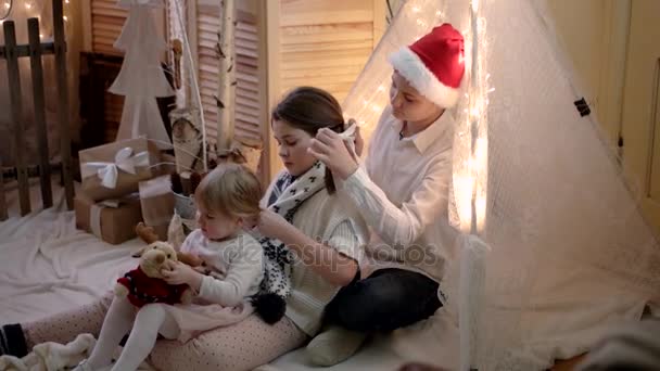 Bruder flechtete seiner kleinen Schwester Zöpfe in Neujahrs- und Weihnachtsdekoration — Stockvideo