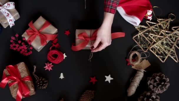 Bovenaanzicht handen inwikkeling Kerstcadeaus op zwarte achtergrond van bovenaf. Cadeau verpakt in bruin papier en gebonden wit lint — Stockvideo