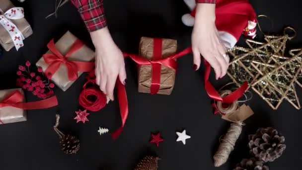 Felülnézet kezek csomagolás karácsonyi ajándékokat a fekete háttér a fenti. Ajándék papírba csomagolva barna és fehér szalaggal kötött — Stock videók