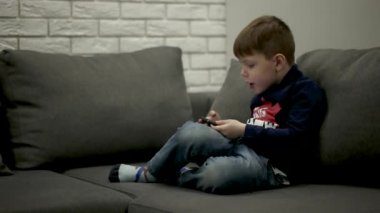 Kanepede oturan ve akıllı telefonda oyunlar oynamak genç çocuk.