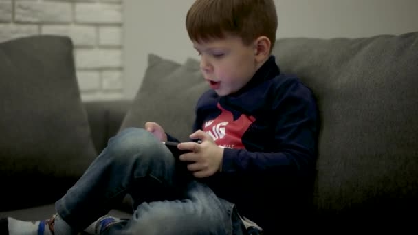 Young Boy Sitting on the Couch and Playing Games on the Smart Phone. — Stock Video