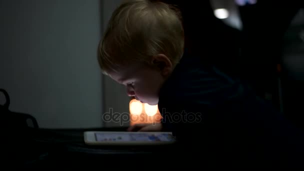 Маленький мальчик смотрит мультики в планшете поздно вечером крупным планом лицо — стоковое видео