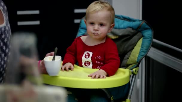 Moeder haar babyjongen met een lepel voeden. Moeder voedsel te geven aan haar schattige twee jaar oud kind — Stockvideo