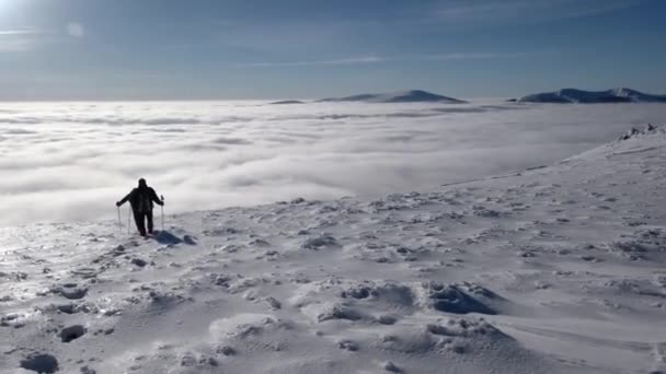 Viajeros con mochilas hacen una caminata de invierno por encima de las nubes con una vista de los picos distantes junto a una costa del mar nuboso — Vídeo de stock