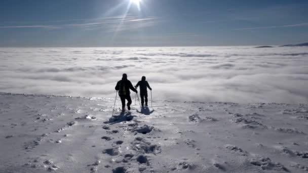 Путешественники с рюкзаками совершить зимний поход над облаками с видом на отдаленные вершины на побережье облачного моря — стоковое видео