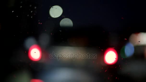 Podczas jazdy w nocy. Widok pękającej przedniej szyby i niewyraźne samochodów w mieście. Rozmyte i deszczowa widok z okna samochodu — Wideo stockowe