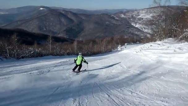 Vista trasera en cámara lenta del esquiador profesional tallando por la ladera nevada — Vídeo de stock