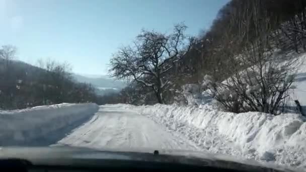 Het besturen van een auto op landelijke land weg in de Winter. Sneeuw en ijs op de snelweg en in de buurt van bergen en heuvels. Oogpunt van de eerste persoon door voorruit. — Stockvideo