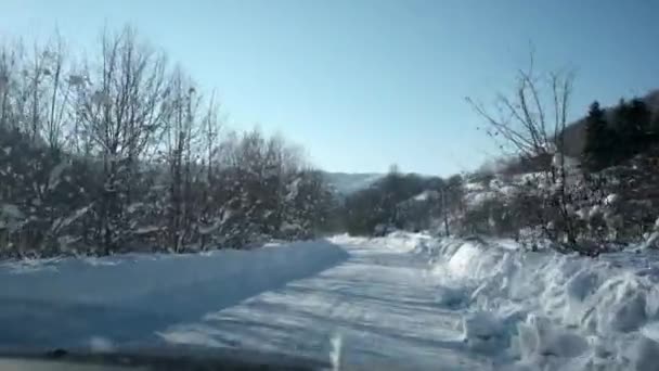 在冬季农村的乡村道路上驾驶一辆车。雪和冰在高速公路和附近的山地和丘陵。第一人称的角度通过挡风玻璃. — 图库视频影像