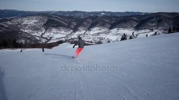 Vista trasera en cámara lenta del esquiador profesional tallando por la ladera nevada — Vídeo de stock