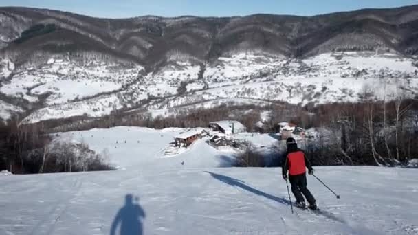 Vista trasera en cámara lenta del esquiador profesional tallando por la ladera nevada — Vídeos de Stock