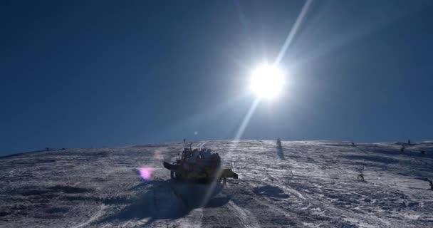 Skifahrer auf dem Rücken einer Pistenraupe auf einem schneebedeckten Berg an einem sonnigen Wintertag — Stockvideo