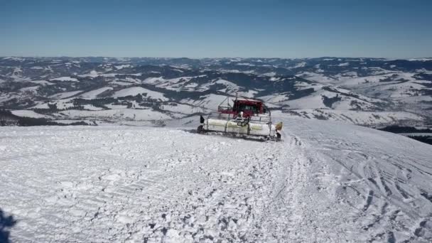 Skifahrer auf dem Rücken einer Pistenraupe auf einem schneebedeckten Berg an einem sonnigen Wintertag