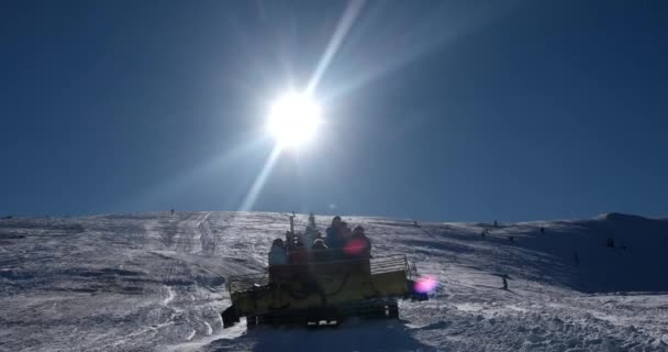 Skiërs rijden op de rug van een Snowcat op een sneeuw bedekt berg op een zonnige winterdag — Stockvideo