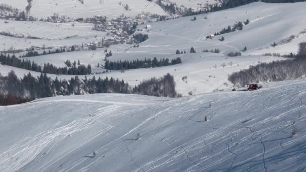 Snowcat con esquiadores en la espalda montando en una colina cubierta de nieve en un día soleado de invierno — Vídeos de Stock