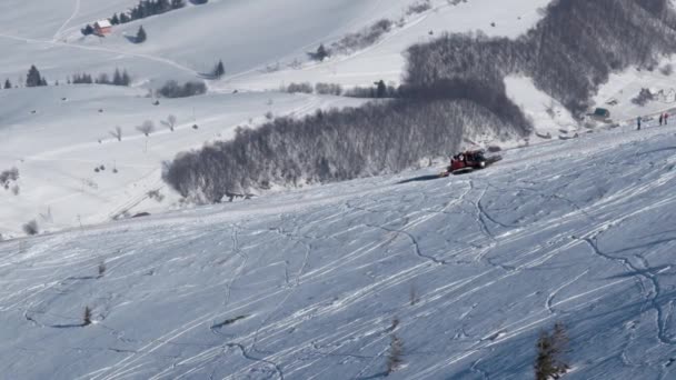 Gato de neve com esquiadores nas costas cavalgando em uma montanha coberta de neve em um dia ensolarado de inverno — Vídeo de Stock
