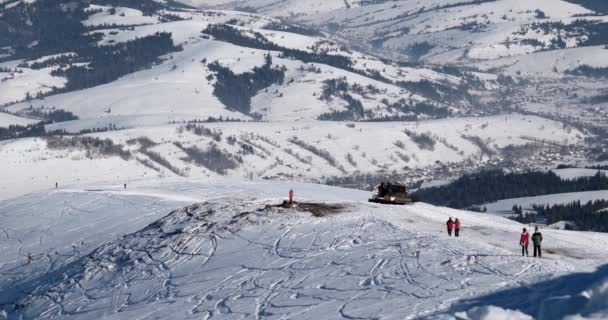 Snowcat mit Skifahrern auf dem Rücken, die an einem sonnigen Wintertag auf einem schneebedeckten Berg reiten — Stockvideo