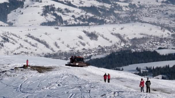 Snowcat mit Skifahrern auf dem Rücken, die an einem sonnigen Wintertag auf einem schneebedeckten Berg reiten — Stockvideo