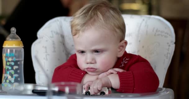 Menino brincando com um carro de brinquedo, sentado em uma cadeira de bebê — Vídeo de Stock