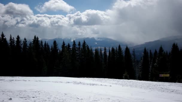 Vinterlandskab med træer, sneklædte bjerge og skyer, vinden blæser væk sneen – Stock-video