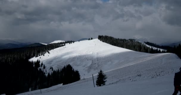 Winterlandschaft mit Bäumen, schneebedeckten Bergen und Wolken, der Wind verweht den Schnee — Stockvideo