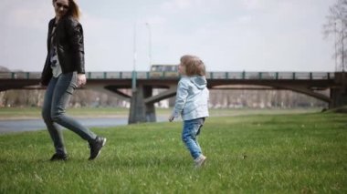 Ona sarılmak için annenin eline çalıştıran ve etrafında dönen çocuk. Aile yeşil çimenlerin üzerinde parkta eğleniyor. Ağır çekim