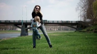 Ona sarılmak için annenin eline çalıştıran ve etrafında dönen çocuk. Aile yeşil çimenlerin üzerinde parkta eğleniyor. Ağır çekim