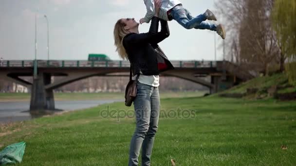 Ребенок бежит в руки матери, чтобы обнять ее и вращаться. Семья развлекается в парке на зеленой траве. Slow Motion — стоковое видео