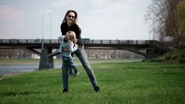 Niño corriendo hacia las manos de la madre para abrazarla y dar vueltas. Familia divirtiéndose en el parque en una hierba verde. Moción lenta — Vídeos de Stock