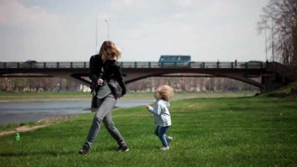 Ona sarılmak için annenin eline çalıştıran ve etrafında dönen çocuk. Aile yeşil çimenlerin üzerinde parkta eğleniyor. Ağır çekim — Stok video