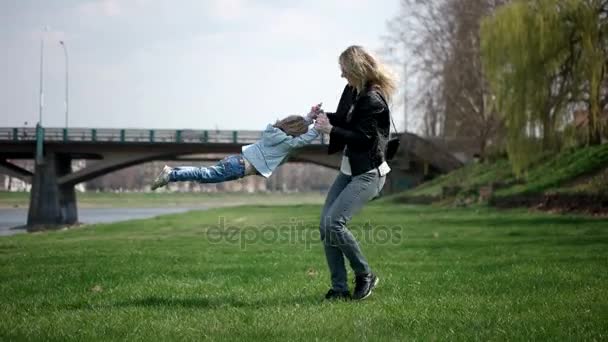 Criança correndo para as mãos da mãe para abraçá-la e girar ao redor. Família se divertindo no parque em uma grama verde. Movimento lento — Vídeo de Stock
