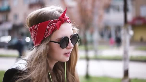 Adolescente chica casual en gafas de sol montando su bicicleta a través de la ciudad y escuchar la música con auriculares — Vídeos de Stock