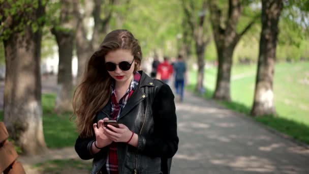 Ragazza hipster casual adolescente urbana in occhiali da sole utilizzando uno smartphone mentre in piedi sulla passerella della città — Video Stock