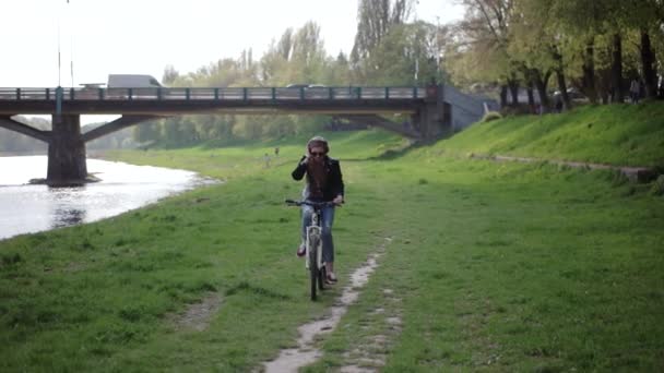 Urbano adolescente casual hipster chica con en gafas de sol montando su bicicleta cerca del río — Vídeo de stock