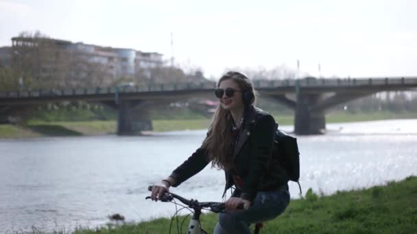 Urbano adolescente Casual Hipster menina com em óculos de sol montando sua bicicleta perto do rio — Vídeo de Stock