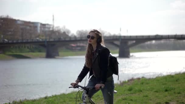 Urbano adolescente casual hipster ragazza con in occhiali da sole cavalcando la sua bicicletta vicino al fiume — Video Stock