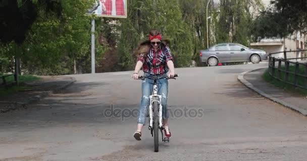 Casual tonårsflicka i solglasögon ridning hennes cykel genom staden — Stockvideo