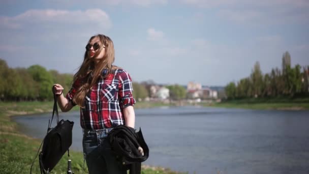 Tizenéves lány alkalmi napszemüveg élvezi a kilátást a folyó közelében, egy napsütéses napon — Stock videók