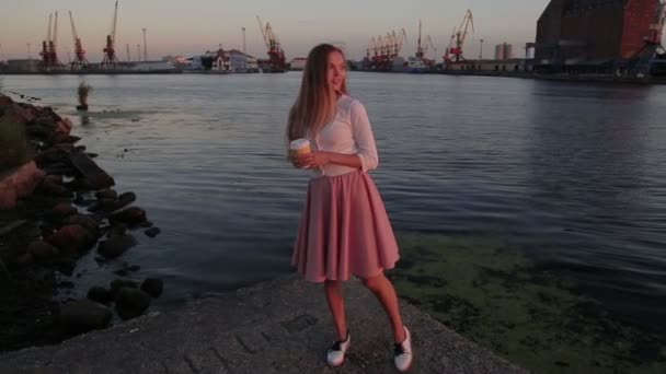 Жінка п'є каву спостерігаючи за заходом сонця стрибає і танцює річковий порт — стокове відео