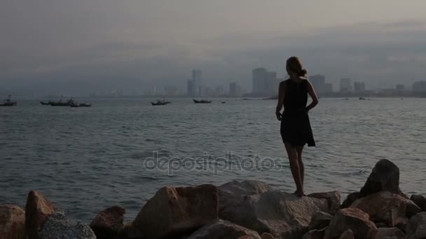 Taşlar üzerinde sahilde duran ve denizde izlerken genç kadın — Stok video